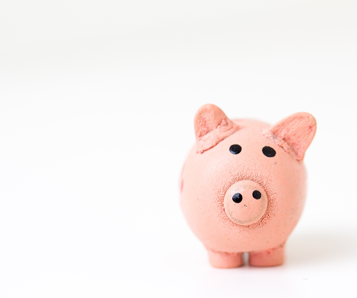 Pink handmade piggy bank on white surface and background; highlighting the financial considerations in buying and selling simultaneously