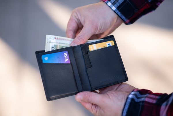 A closeup of a mans hands holding a wallet, pulling out cash with credit cards in the wallet slots; highlighting the debt service ratio in reference to mortgages