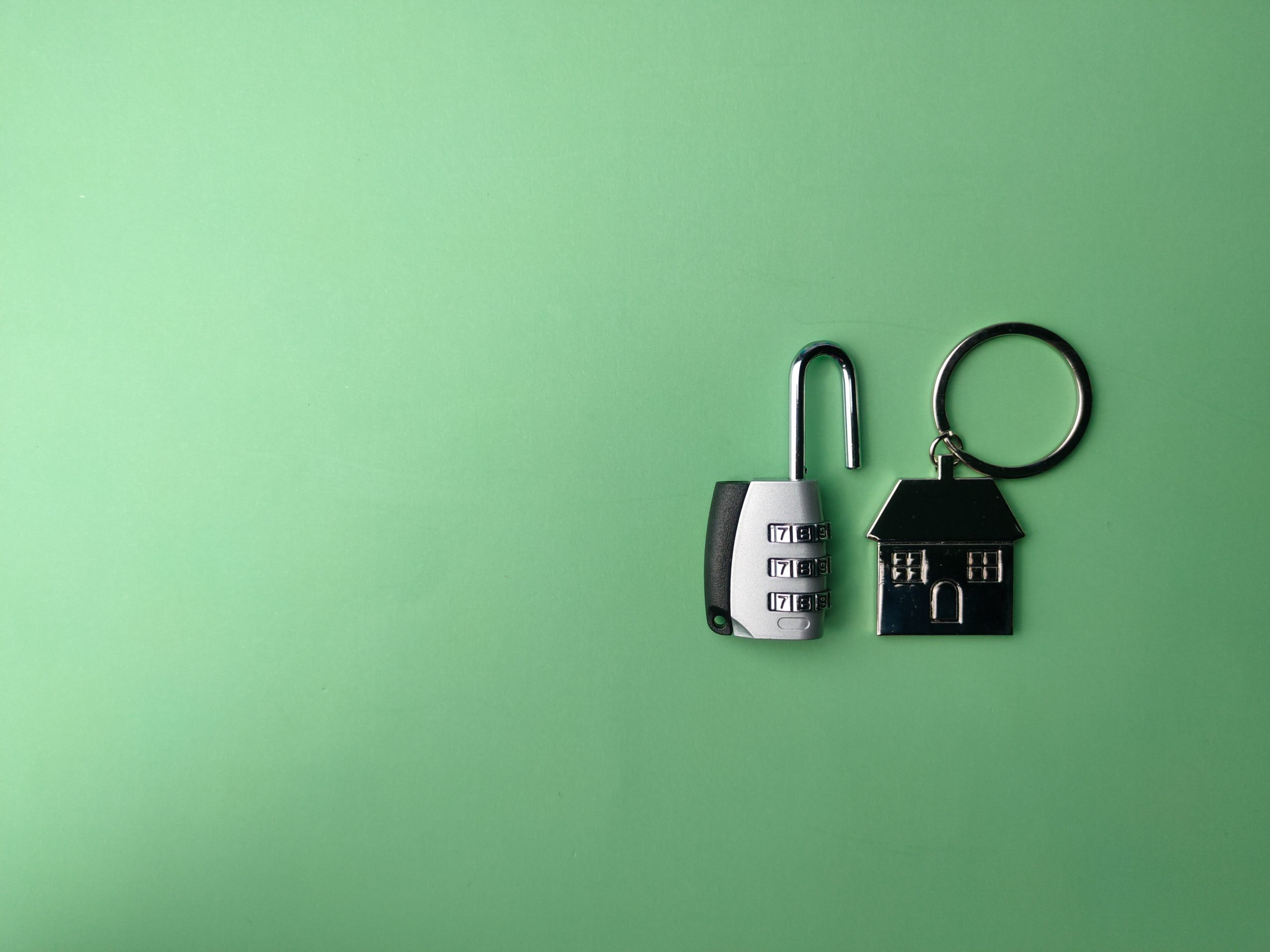 a metal keychain of a house with an opened lock next to it on a light green background
