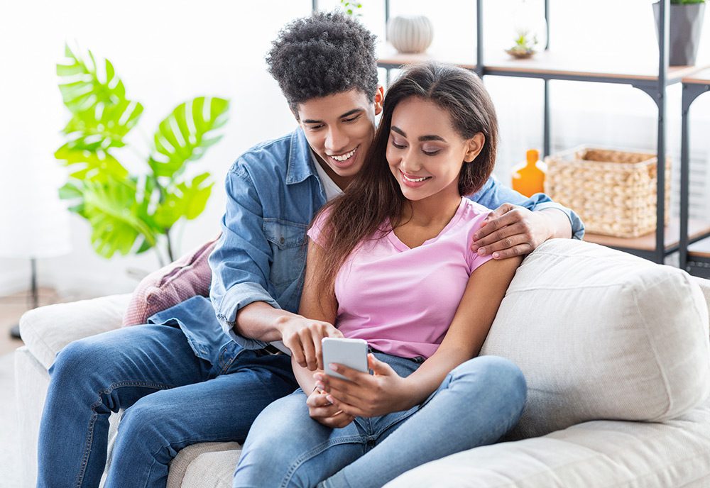 A young couple sitting on the couch and looking at mortgage information on their phone