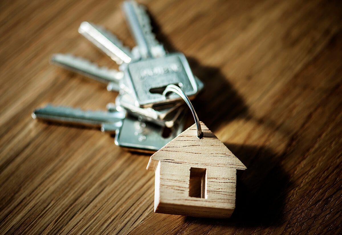 a set of keys on a wooden surface with a wooden house keyring, referencing using a mortgage broker to buy a new home